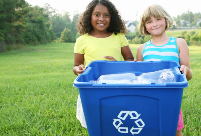 two young girls hold a recycling bin