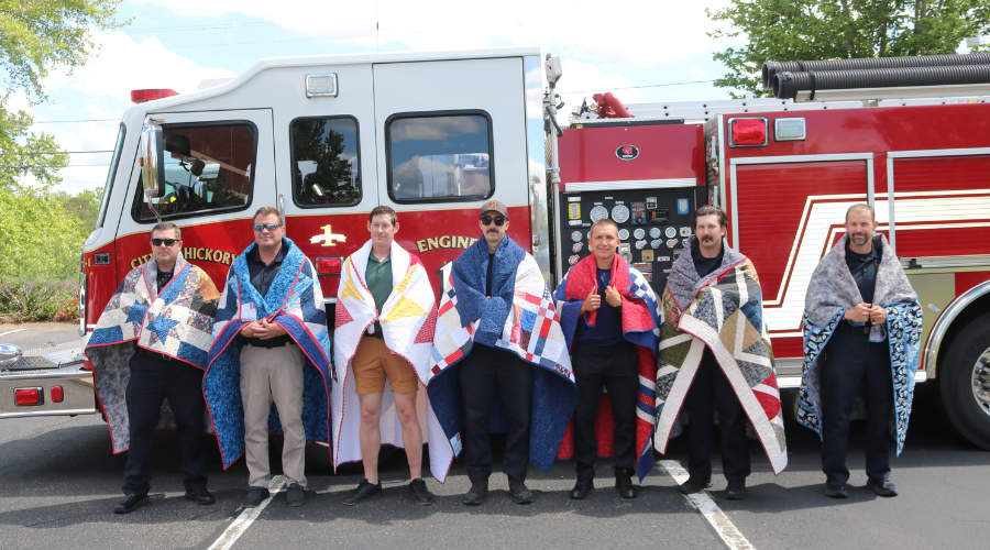 Hickory firefighters wrapped in quilts stand in front of a firetruck