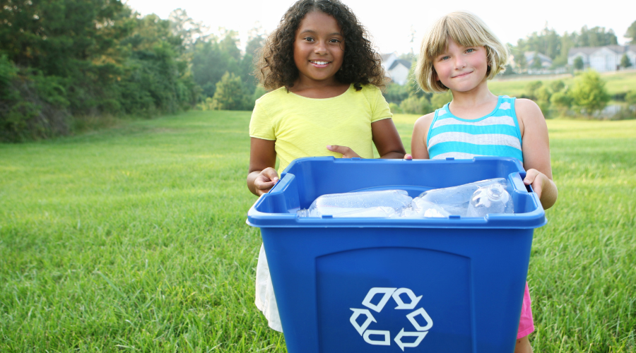 two young girls hold a recycling bin